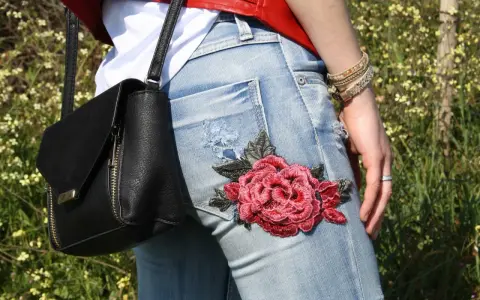 Detalle de unos pantalones vaqueros con un llamativo bordado de rosa roja, perfectos para tunear tus vaqueros y darle un toque único.