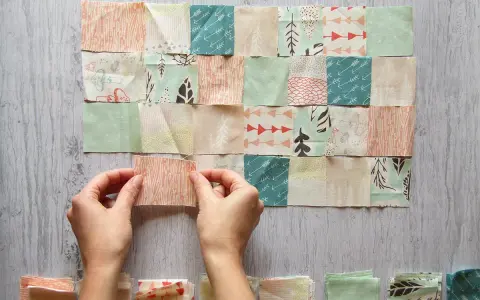 Manos uniendo retazos de tela con diseños de árboles y flechas, creando un patrón de patchwork.