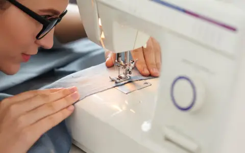 Mujer con gafas concentrada en sus proyectos de costura, cosiendo tela azul en una máquina de coser.