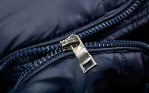 Enganche cremallera roto en chaqueta azul marino. El tirador metálico está desprendido, dejando la cremallera inutilizable.