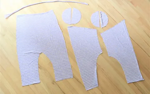 Piezas de tela a rayas lilas, listas para coser un patrón de peto para bebé.