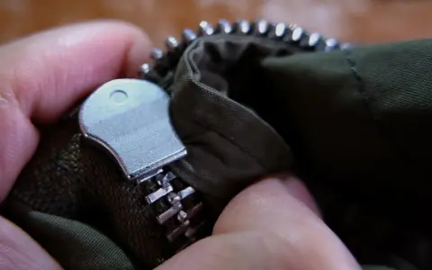 Mano arreglando cremallera doble carro de chaqueta verde.