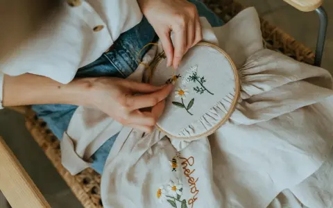 Manos bordando flores y una abeja en tela. El bordado con lana le da un toque artesanal y delicado a la pieza.