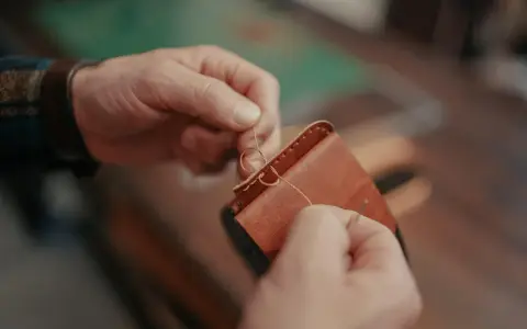 Manos cosiendo a mano un monedero de cuero. Se aprecian los detalles de los tipos de costuras de cuero a mano.