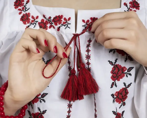 Manos atando cordones rojos en una blusa blanca con **bordado digital** de flores rojas y negras.