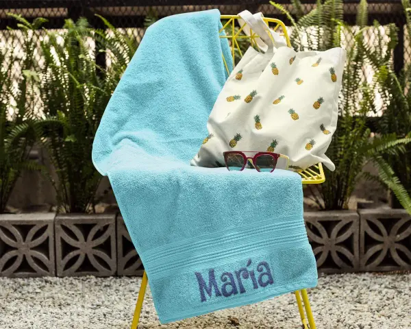 Toalla turquesa con el nombre "María" bordado, lista para la playa.