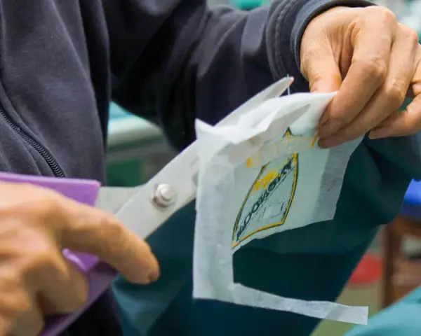 Manos cortan con tijeras un parche bordado sobre tela estabilizadora, preparándolo para ser cosido.