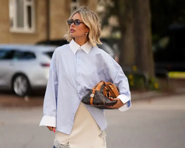 Mujer con camisa oversize azul, falda lencera de encaje y bolso de diseño. Un look para tunear ropa de mujer con estilo.