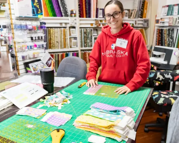Mujer sonriente en tienda de telas, rodeada de retazos y herramientas de costura.