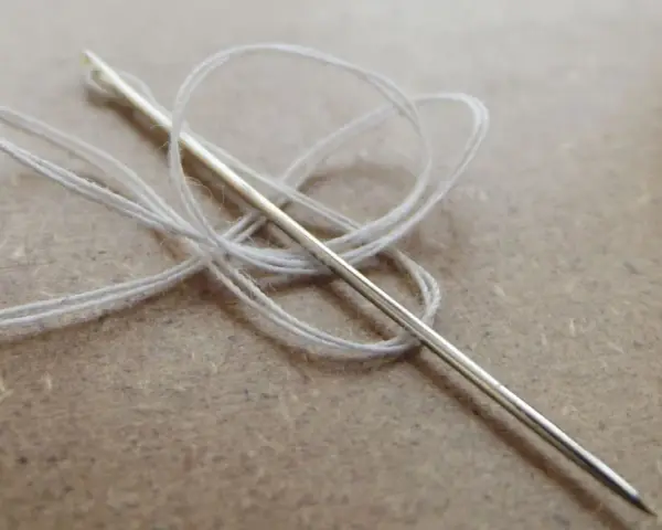 Aguja con hilo blanco enredado, lista para coser a punto de lado.