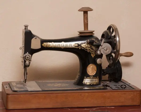 Máquina de coser Singer antigua, pieza clave en la historia de la costura, con detalles dorados y base de madera.