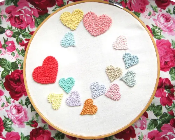 Un aro de bordar muestra un montón de corazones bordados de colores, como un arcoíris de amor.