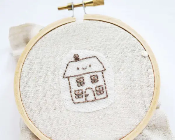 Bordado de una casita sonriente sobre papel para bordar que se deshace con el agua.