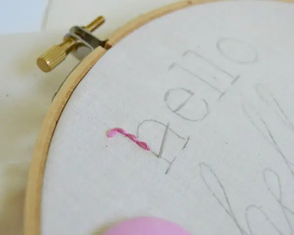 Bastidor con tela y un hilo rosa comenzando a bordar letras.