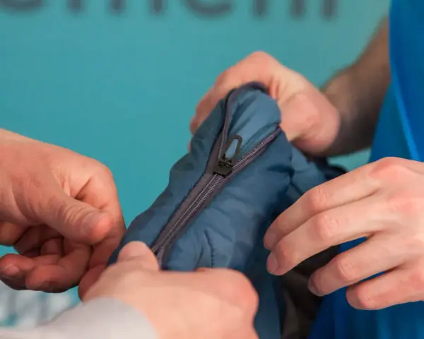 Manos intentan arreglar pistón cremallera de un saco de dormir azul.