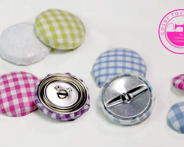 Botones forrados con tela de cuadros vichy en rosa, morado, verde y azul. Se ven los cierres metálicos.