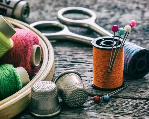 Herramientas para arreglar una ropa con un trozo del mismo tipo: hilos de colores, tijeras, dedales y alfileres.