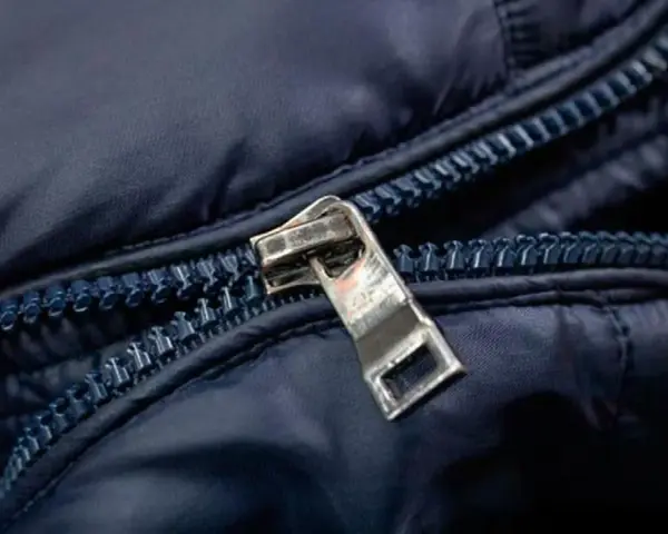 Enganche cremallera roto en chaqueta azul marino. El tirador metálico está desprendido, dejando la cremallera inutilizable.