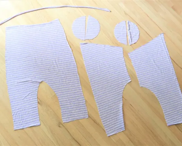 Piezas de tela a rayas lilas, listas para coser un patrón de peto para bebé.