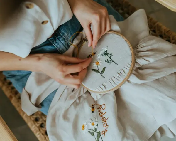 Manos bordando flores y una abeja en tela. El bordado con lana le da un toque artesanal y delicado a la pieza.