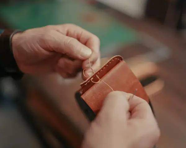 Manos cosiendo a mano un monedero de cuero. Se aprecian los detalles de los tipos de costuras de cuero a mano.