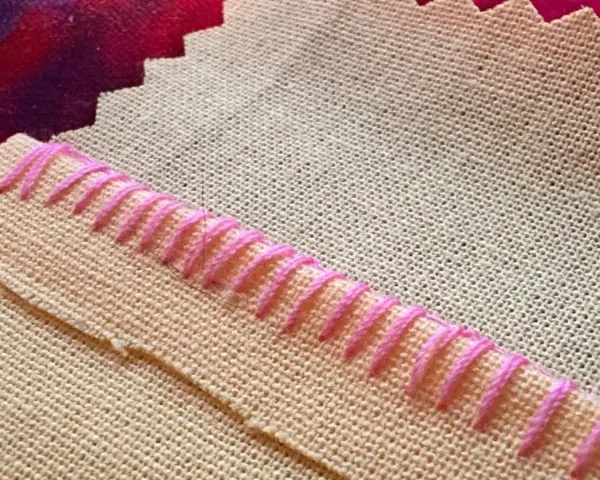 Detalle de tela beige con puntada de hilo rosa formando un borde decorativo.