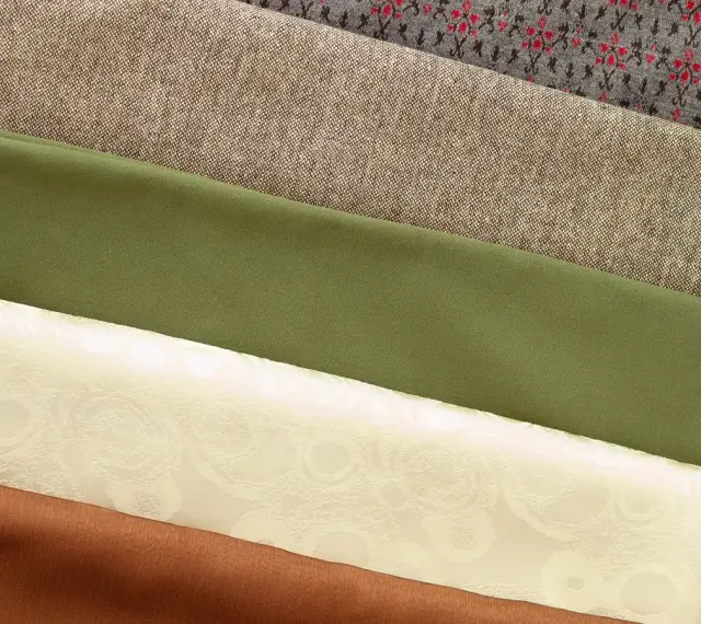 Variedad de tipos de tela apiladas: gris con patrón, beige texturizado, verde liso, crema con relieve floral y marrón.