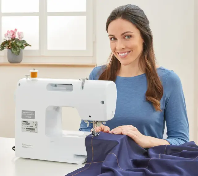 Mujer sonriente cosiendo a maquina una tela azul.
