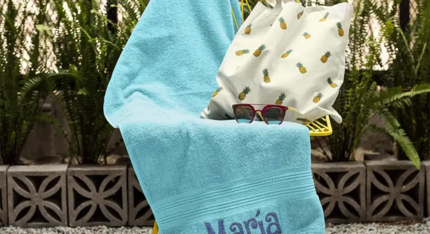 Toalla turquesa con el nombre "María" bordado, lista para la playa.