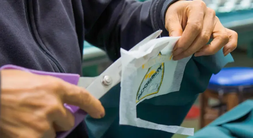 Manos cortan con tijeras un parche bordado sobre tela estabilizadora, preparándolo para ser cosido.
