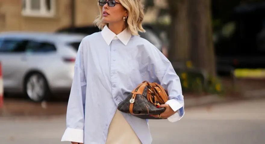 Mujer con camisa oversize azul, falda lencera de encaje y bolso de diseño. Un look para tunear ropa de mujer con estilo.