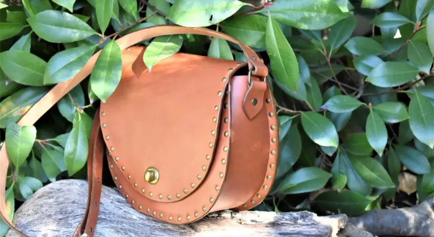 Bolso de cuero marrón con tachuelas, ideal para quienes buscan patrones de bolsos gratis para descargar y crear sus propios accesorios.