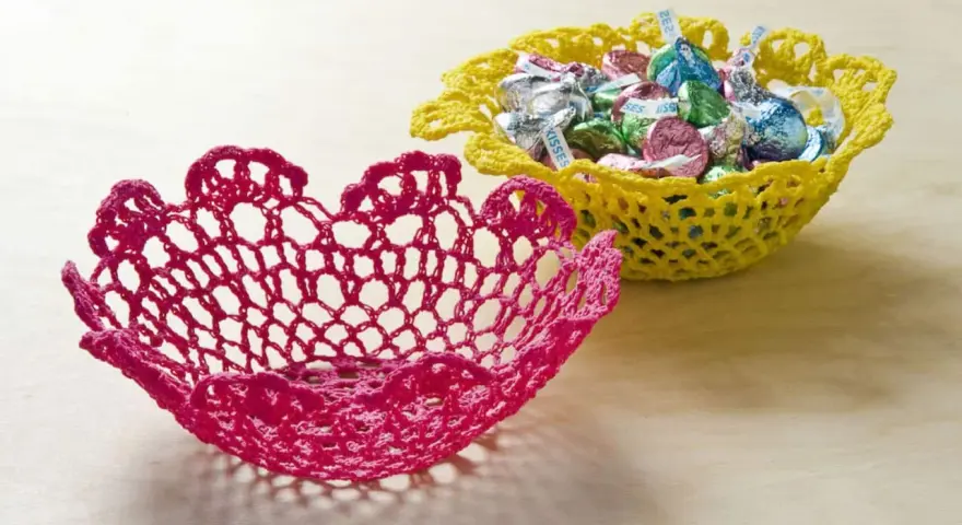 Dos cuencos de ganchillo, uno rosa y otro amarillo lleno de caramelos. Aprende como dar rigidez a una tela para crear estas piezas decorativas.
