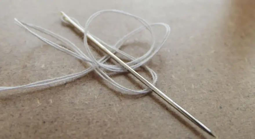 Aguja con hilo blanco enredado, lista para coser a punto de lado.