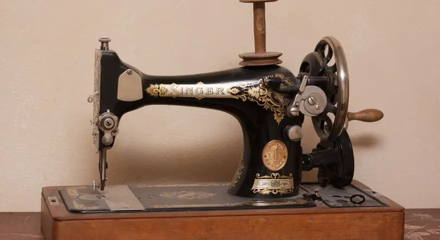 Máquina de coser Singer antigua, pieza clave en la historia de la costura, con detalles dorados y base de madera.