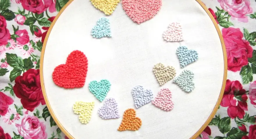 Un aro de bordar muestra un montón de corazones bordados de colores, como un arcoíris de amor.