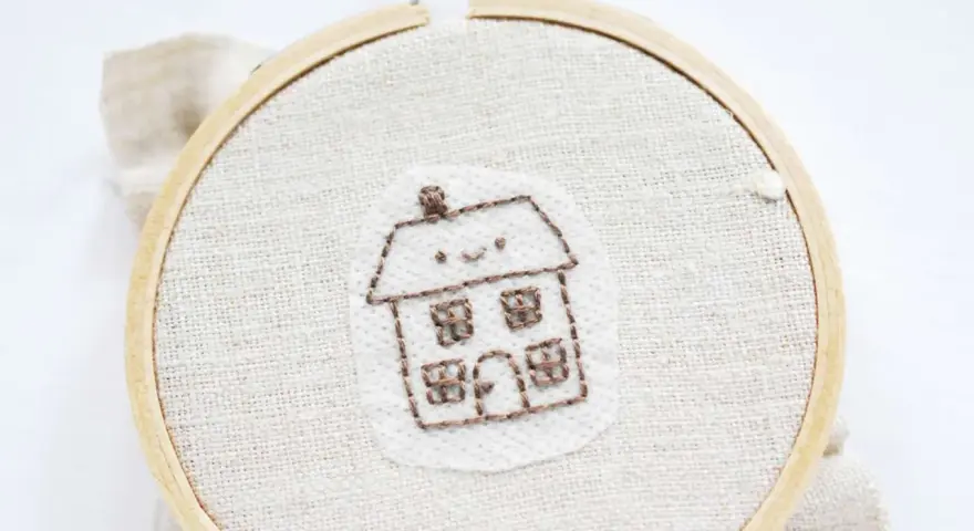 Bordado de una casita sonriente sobre papel para bordar que se deshace con el agua.