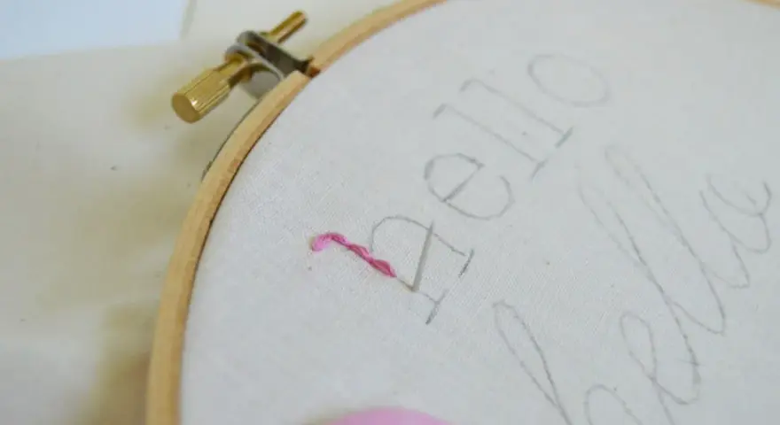 Bastidor con tela y un hilo rosa comenzando a bordar letras.