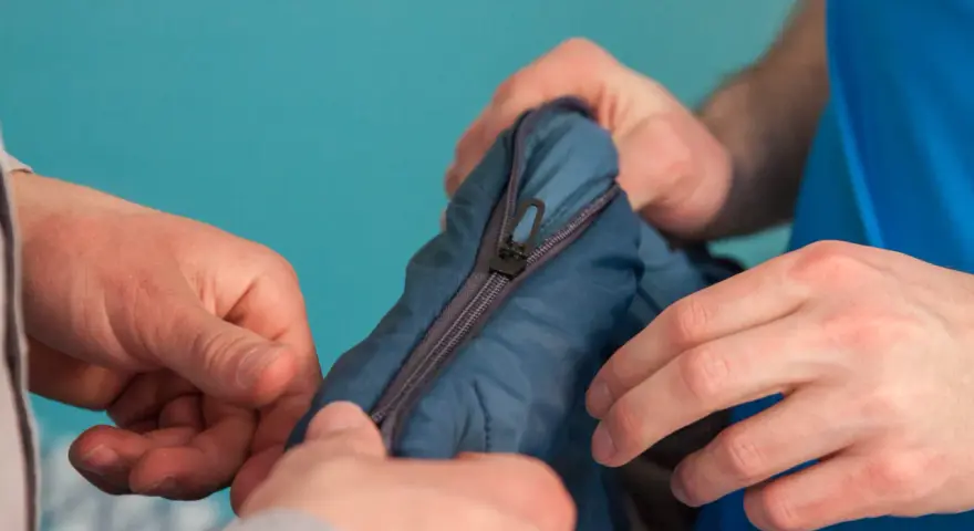 Manos intentan arreglar pistón cremallera de un saco de dormir azul.