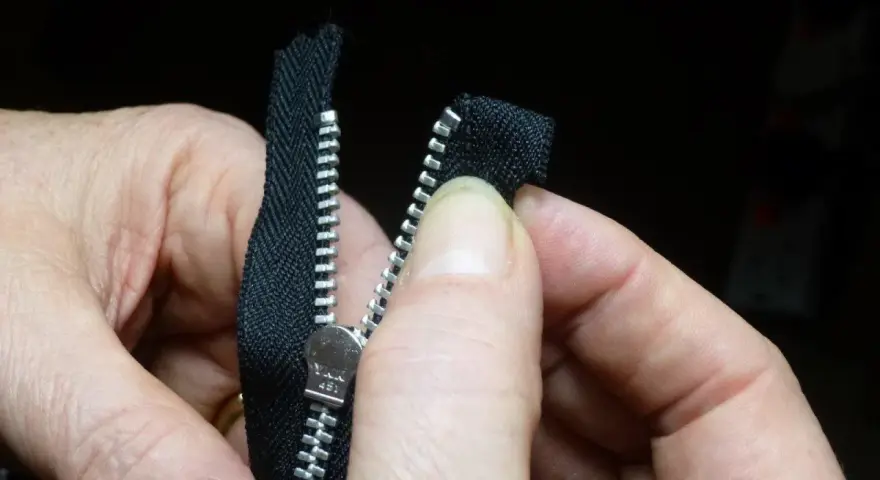 Manos sujetan una cremallera negra, alineando los dientes para coser cremallera a mano.