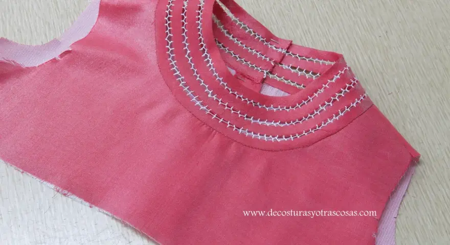 Detalle de camiseta rosa con bordado a mano en el cuello, creando un diseño delicado y único.