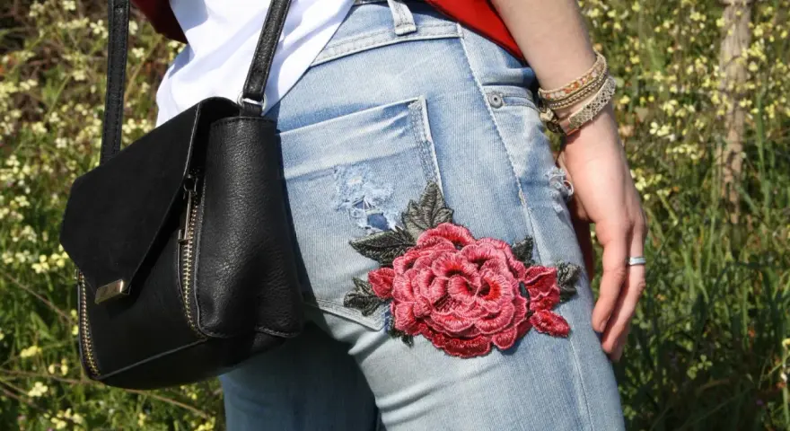 Detalle de unos pantalones vaqueros con un llamativo bordado de rosa roja, perfectos para tunear tus vaqueros y darle un toque único.