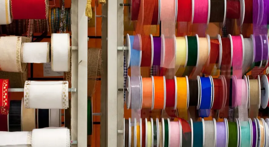 Variedad de tipos de cintas de tela en rollos, con colores y texturas diversas, ideales para manualidades y decoración.