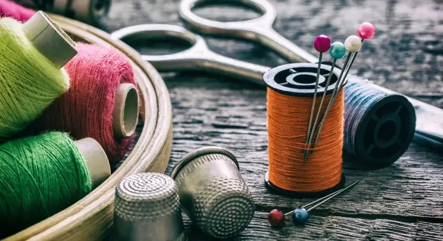 Herramientas para arreglar una ropa con un trozo del mismo tipo: hilos de colores, tijeras, dedales y alfileres.