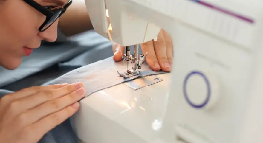 Mujer con gafas concentrada en sus proyectos de costura, cosiendo tela azul en una máquina de coser.