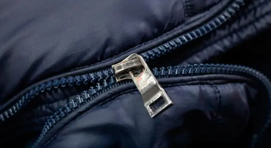 Enganche cremallera roto en chaqueta azul marino. El tirador metálico está desprendido, dejando la cremallera inutilizable.