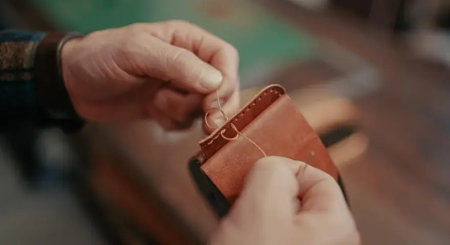 Manos cosiendo a mano un monedero de cuero. Se aprecian los detalles de los tipos de costuras de cuero a mano.