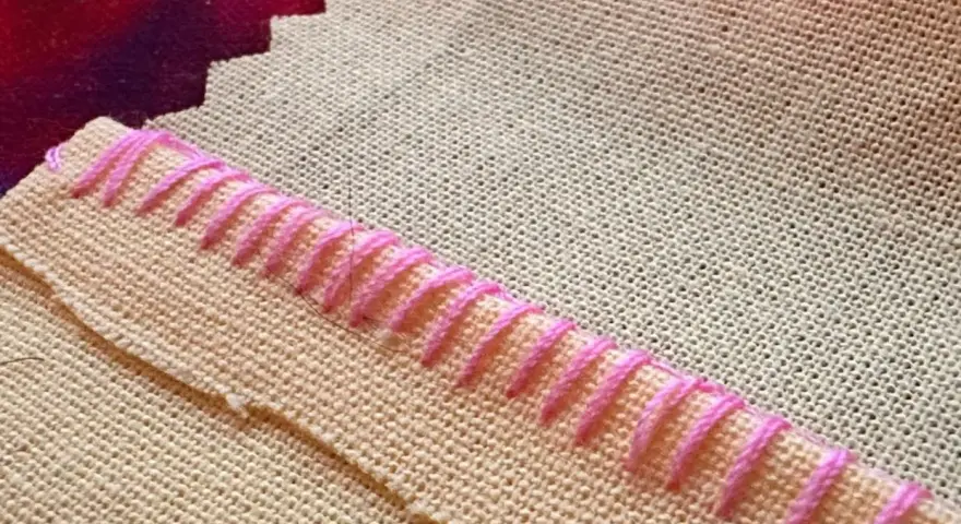 Detalle de tela beige con puntada de hilo rosa formando un borde decorativo.