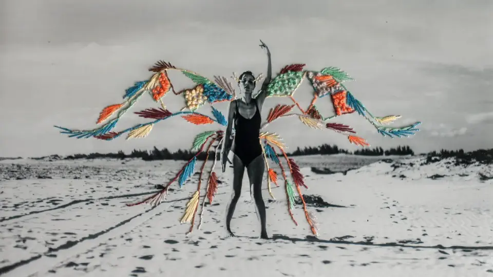 Mujer en traje de baño con alas de bordado de fotos coloridas sobre un paisaje de playa desértica.