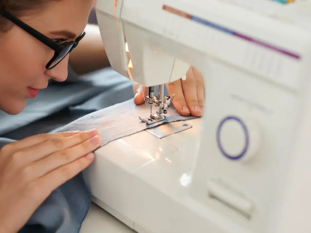 Mujer con gafas concentrada mientras aprende a coser en su m&aacute;quina.